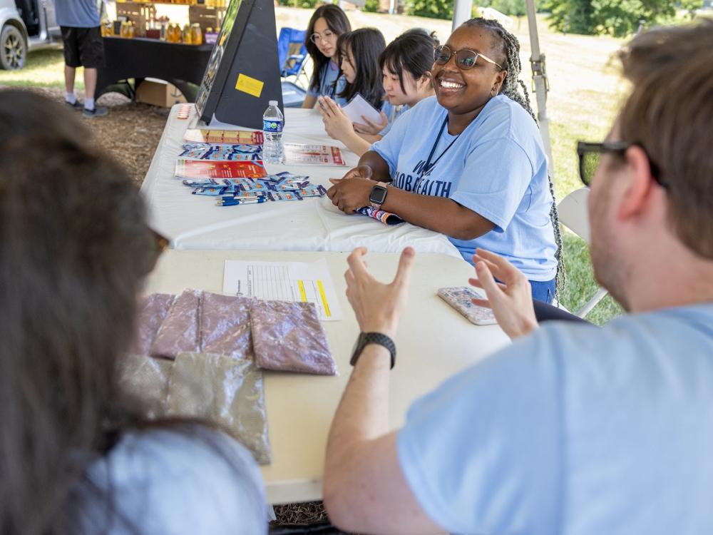 A group of students with matching shirts sit at a stand at a farmer's market