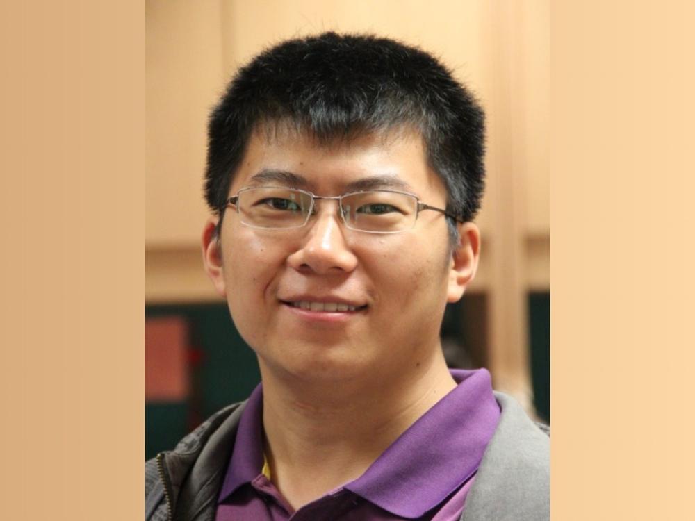 person with dark hair and wire rim glasses wearing purple shirt