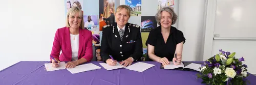 Three women seated at table, signing a document