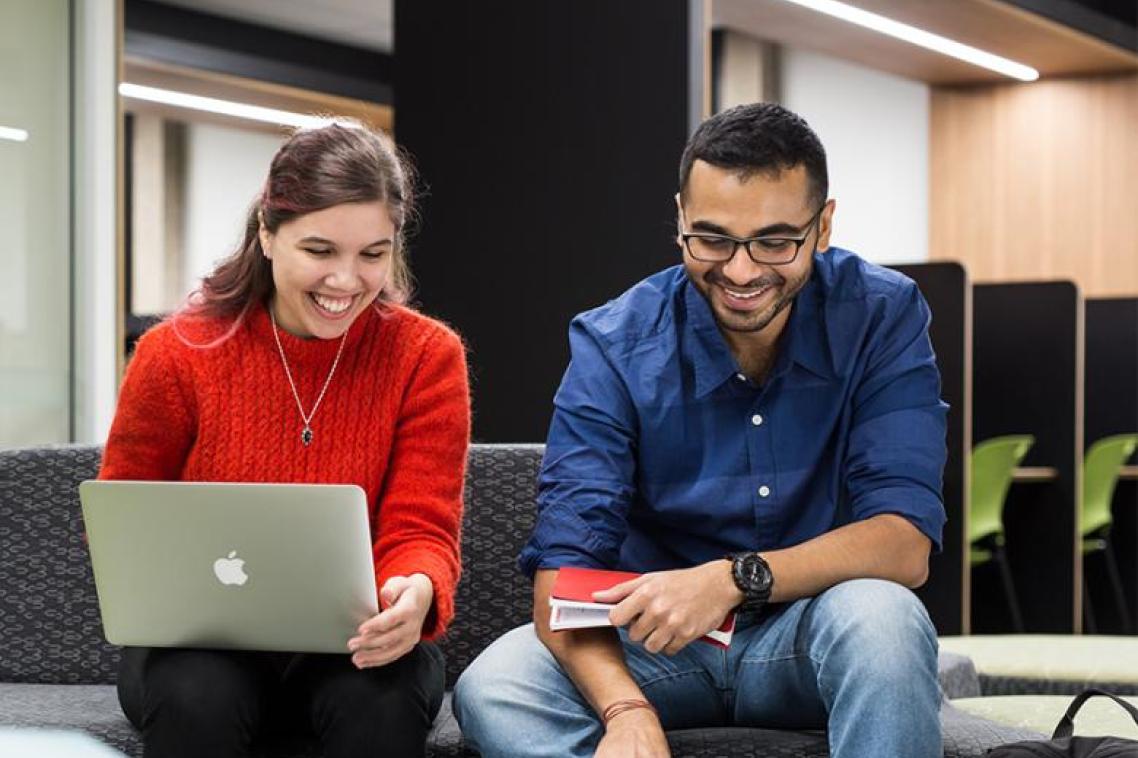 Two students sitting next to each other, one with a laptop. Both are smiling. 