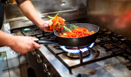 Wok being stirred on a hot stove in a restaurant kitchen.