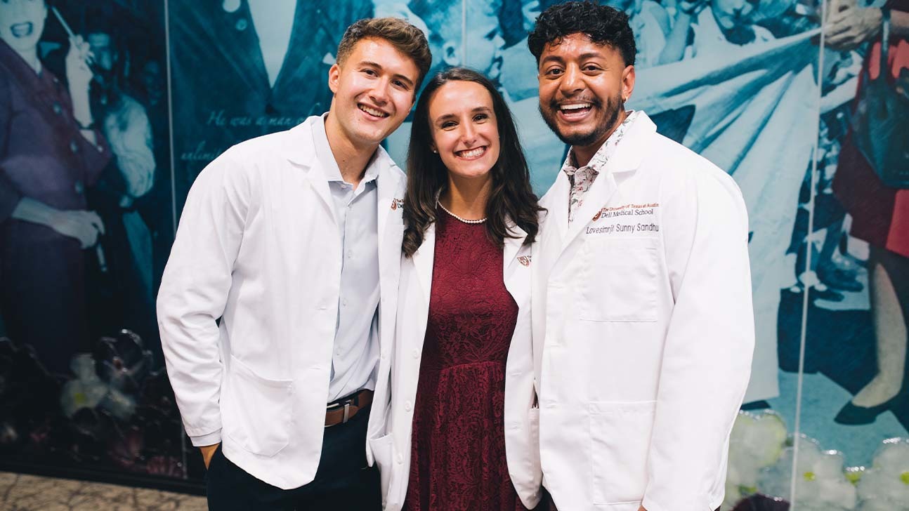 Three medical students, each wearing medical white coats, stand together for a picture.