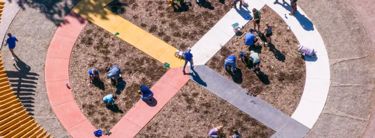 A photo of Čhaŋgléška Wakȟáŋ from above showing the medicine wheel and a number of poeple in the garden enjoying planting