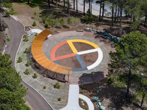 An aerial drone shot of SURF's ethnobotanical garden, Čhaŋgléška Wakȟáŋ, showing the colors of the medicine wheel, a Lakota inspired pergola, and the access road and paths.  