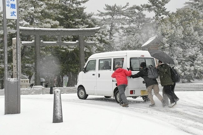 坂道でスリップし、動けなくなった自動車を押す観光客＝７日午前１０時２０分ごろ、出雲市大社町杵築南