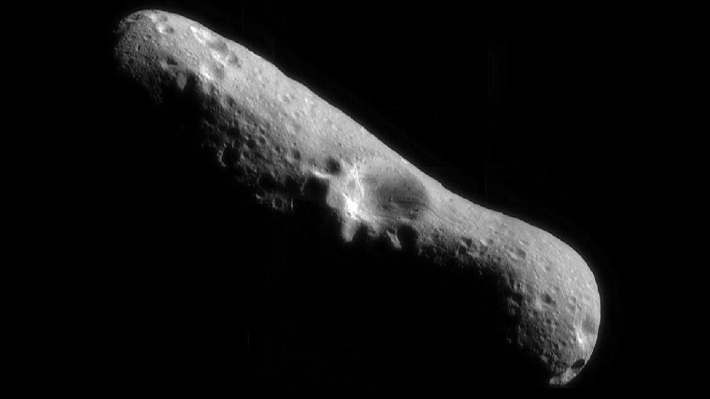 A close-up image of the cigar-shaped asteroid Eros with a large crater near the center.