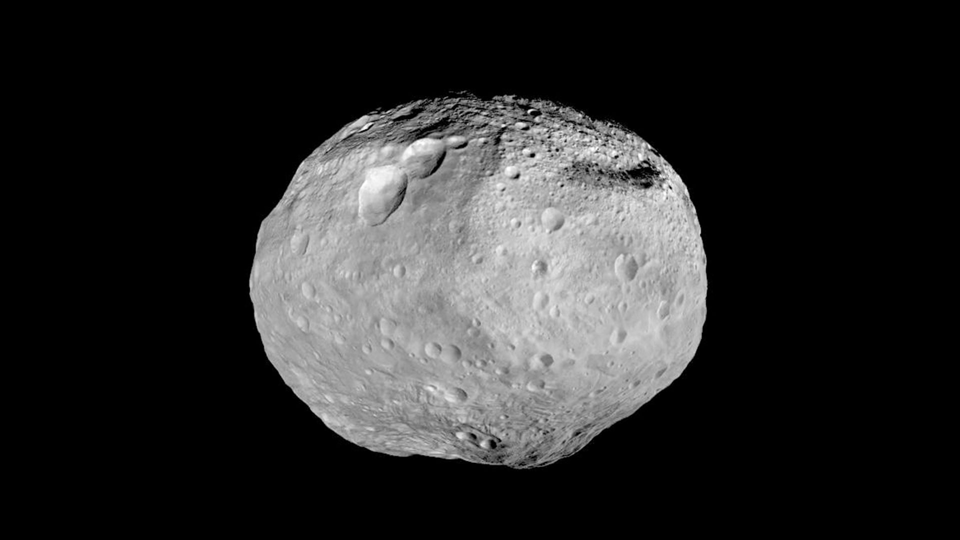 A mostly round asteroid Vesta with large craters visible.