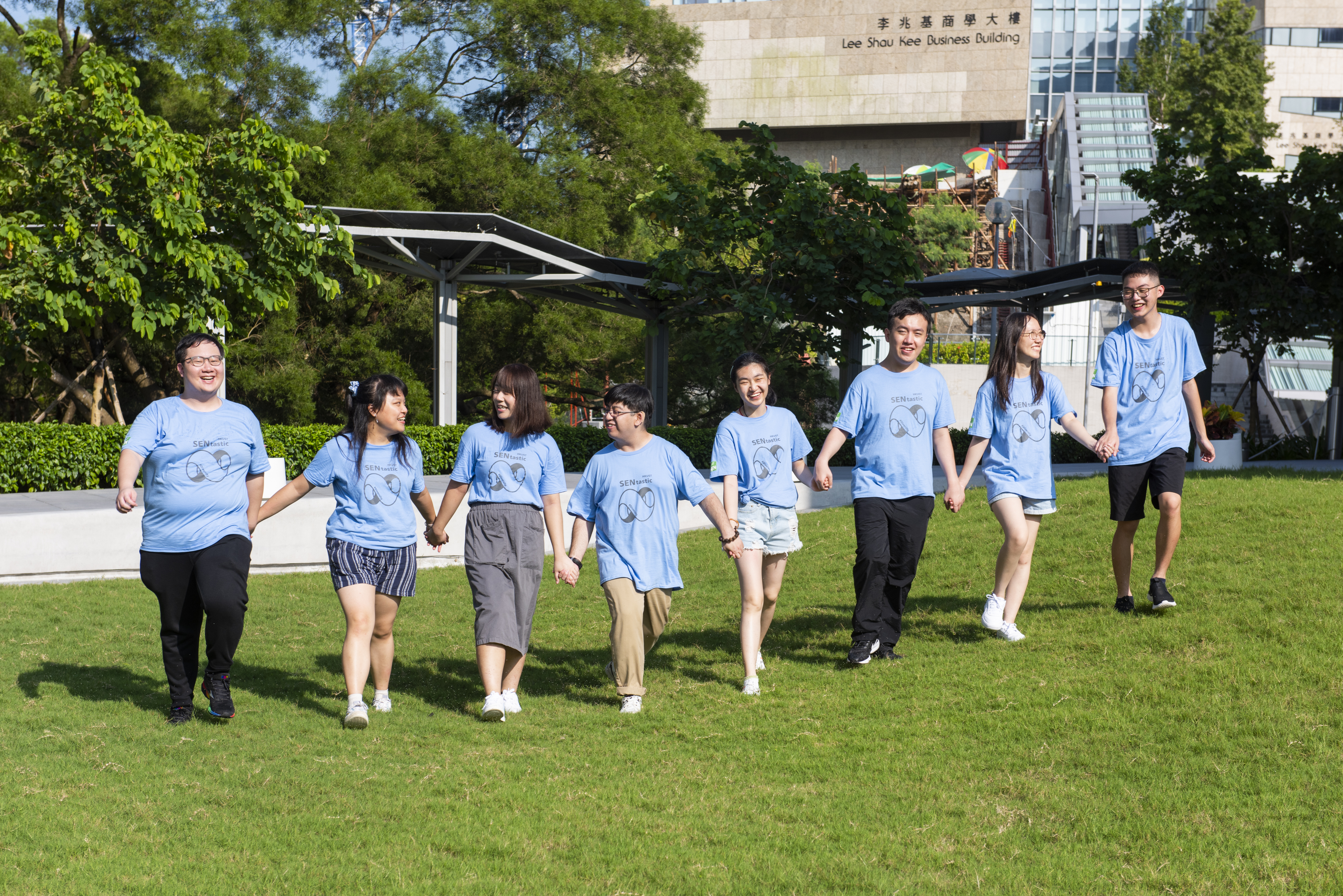 8 students holding hands and walking on grass