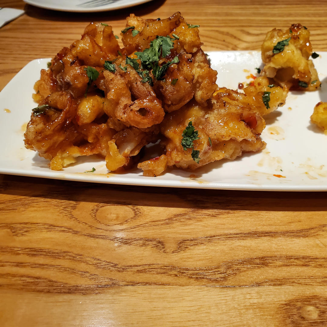 A plate of lightly breaded calamari in a sweet chili-ponzu glaze. Garnished with cilantro and served with sesame-sriracha aioli.