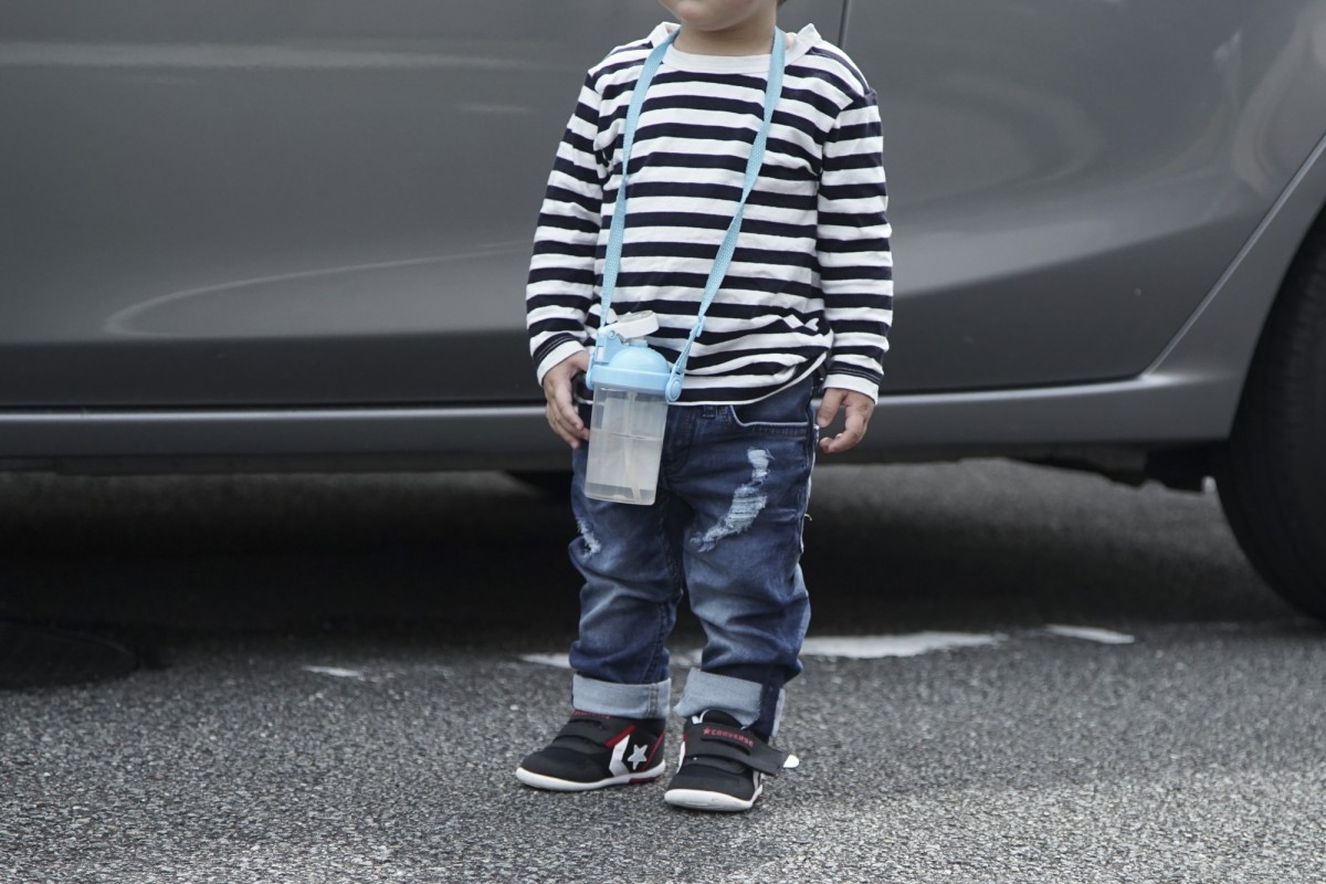 A young boy standing in front of a car