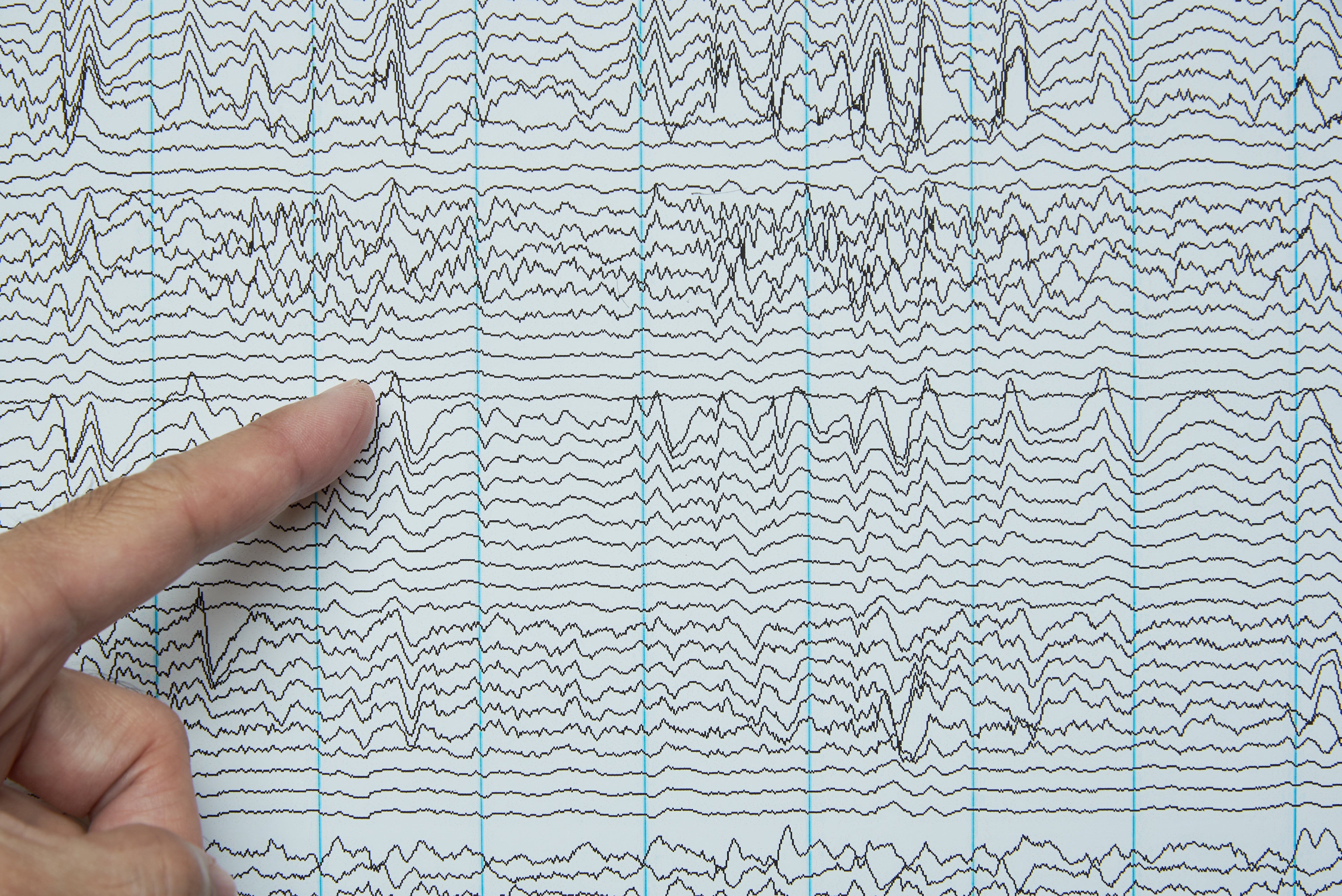 Index finger pointing at imaging of human brain waves from electroencephalography or EEG.