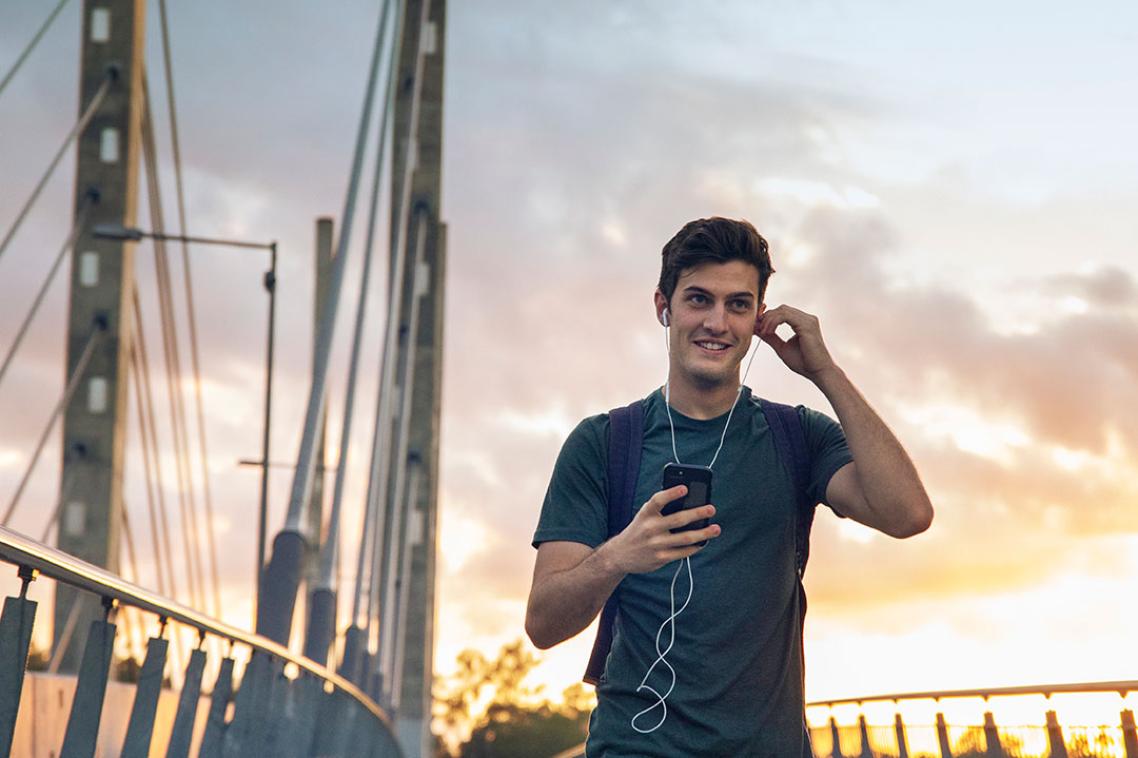 A student walks across the Eleanor Schonell Bridge at sunset.