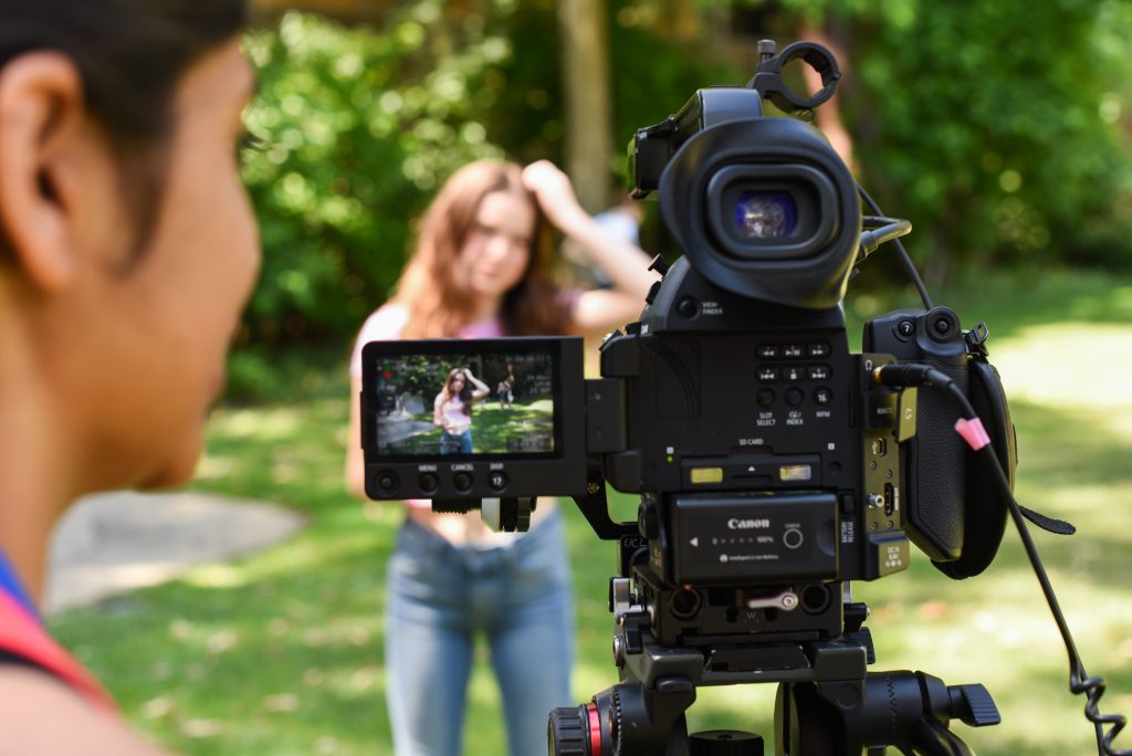 A female student looks at a camera that's facing another female student as the subject, with the subject visible in the camera's preview screen.