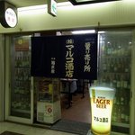 Marco Saketen - お店の概観です。量り売り所　（株）マルコ酒店　って書いていますね。暖簾の横には沢山のお酒が並んでいますよ。暖簾の下から人の足が見えるので混んでいるか混んでいないかは確認できます。