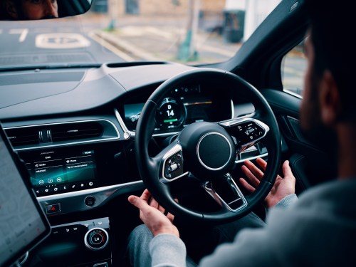 person's hands letting go of steering wheel of self-driving car