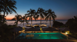 Pool with palm trees by the sea at sunset