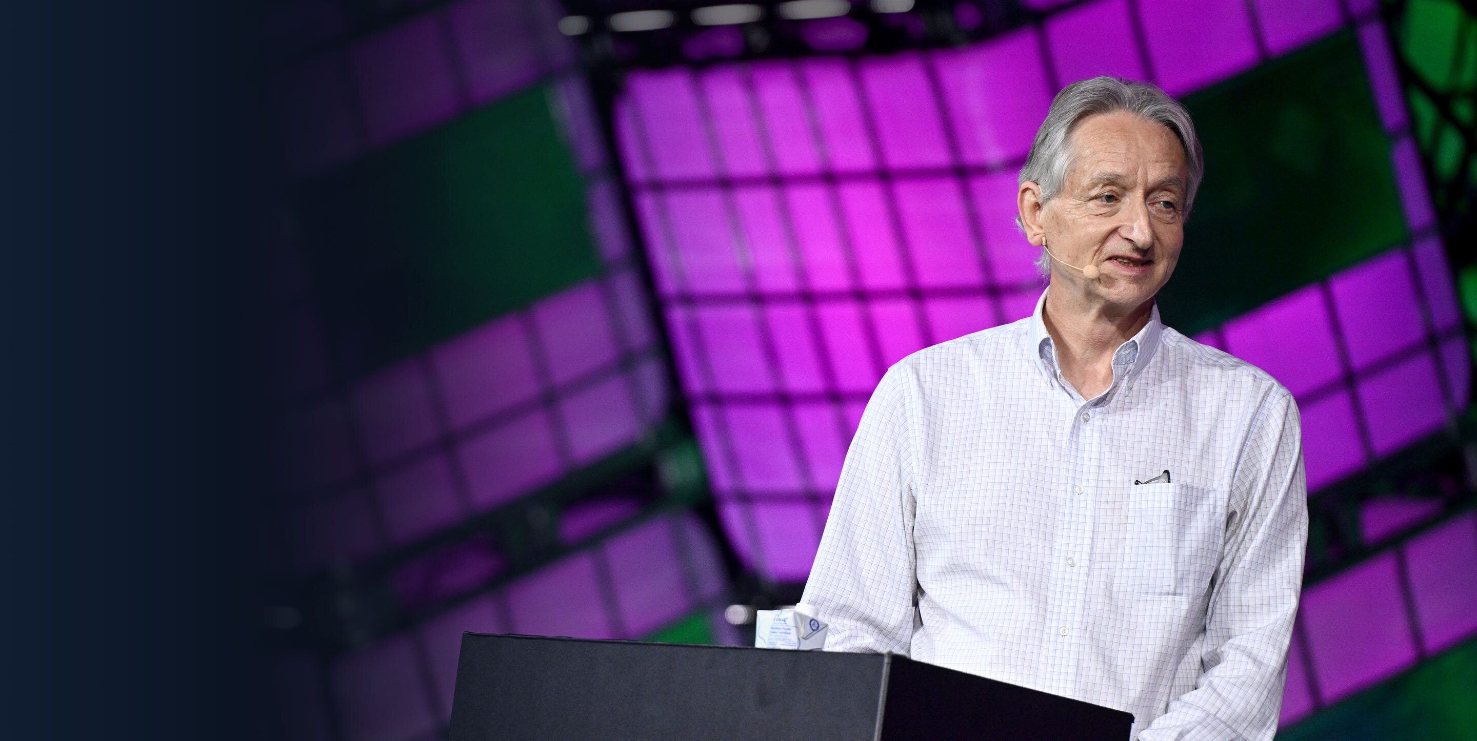 Geoffrey Hinton speaks behind podium against purple background