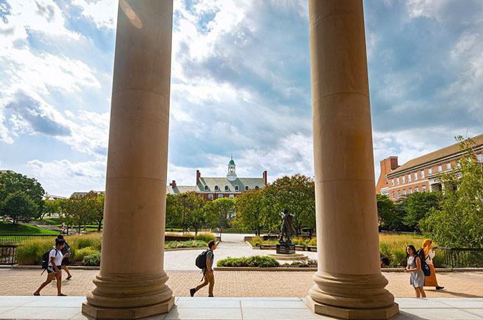 Looking out across Hornbake Plaza, seeing students walk between the pillars of a building at UMD