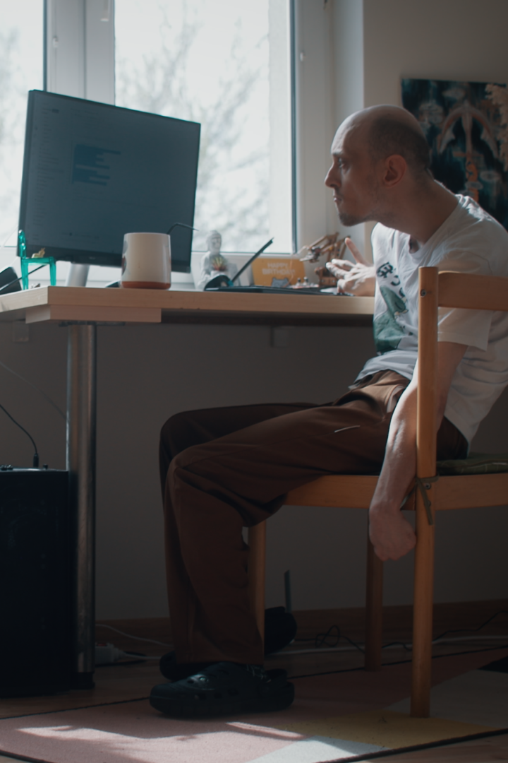 A man sitting at a desk, writing code on a computer. Natural light pours in from large windows.