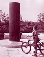 photopgrapie en noir et blanc d'une jeune garçon à bicyclette à côté d'un monument