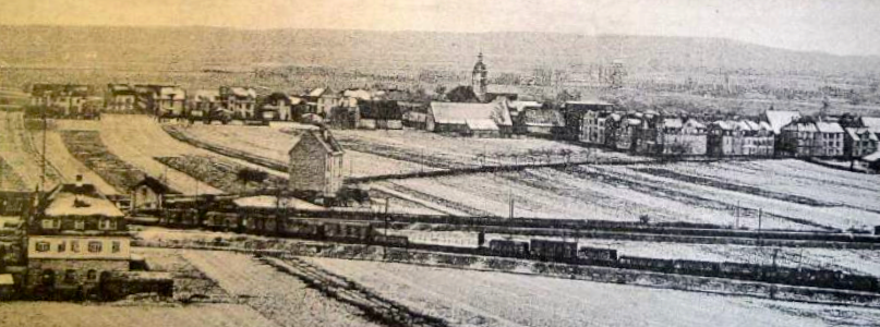 Blick auf das winterliche Oberndorf in den 1910er Jahren, im Hintergrund der Steigerwald. Die Bahnlinie nach Erfurt (vorne) ist die Grenze zwischen den heutige Stadtteilen Oberndorf und Bergl. Die Bahnlinie unmittelbar dahinter führt nach Würzburg. Vorne links ist das Oberndorfer Wasserhaus von 1911 zu sehen und am rechten Ortsrand der Häuserblock Kornstraße/Bismarckstraße (heute Engelbert-Fries-Straße). Unmittelbar links des Hauses hinter den beiden Gleisen verläuft heute die Franz-Josef-Strauß-Brücke (Bahnüberführung). Die Notkirche St. Josef von 1921 (unweit rechts dieses Hauses) stand noch nicht.