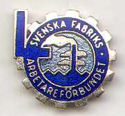 A mainly blue pin badge in the shape of a cog with an L on the left side. the badge depicts a factory chimney bellowing smoke. The writing on the badge says "Svenska Fabriks Arbetare Forbundet" or "Swedish Factory Workers Union" in English.