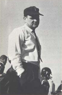 B&W image of man standing wearing a hat, white shirt and non-bowtie.