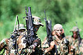 The U.S. Navy SEAL in the foreground is carrying a field radio and is armed with a Colt Model 653 carbine equipped with an M203 grenade launcher.