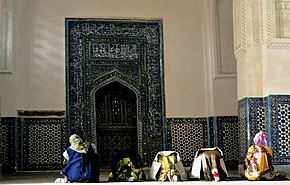 "Beberapa jemaah sedang salat menghadap mihrab atau ceruk yang digunakan imam untuk memimpin salat. Mihrab berwarna hitam dan dihiasi dengan kaligrafi"