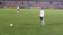 Photographie d'un joueur, portant un maillot blanc, s'apprêtant à tirer un coup franc.