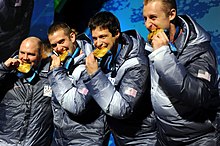 Photographie de quatre hommes tenant en bouche une médaille d'or.