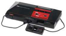 Photo d'une console noire et rouge, à laquelle une manette est branchée
