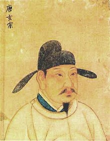detail obrazu císaře Süan-cunga, malba muže středního věku, zachyceno je poprsí, obličej je s malou zastřiženou bradkou a knírem, na hlavě černá čapka s širokýma „ušima“ trčícími do stran, oděv sahaící až ke krku světle žlutý, pozadí také světle žluté poněkud tmavší