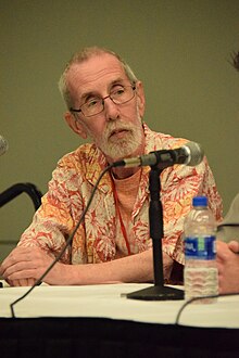 Giffen seated at a panel, wearing a Hawaiin shirt