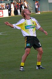 photo d'un footballeur en short noir et maillot blanc et jaune levant la tête en attendant un ballon
