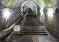 駅地下ホームから長い階段を見上げる。階段左端の岩盤が露出した部分は、将来のエスカレーターの設置のために残されたスペースである。（2021年7月）