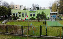zielony, parterowy budynek przedszkola z placem zabaw
