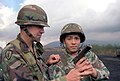 Ausbilder (links) mit der hauptsächlich für den NATO-Einsatz konzipierten „Woodland“-Tarnung an Helm u. Uniform (hier bei der Übung „Orient Shield '85.“)