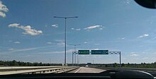 Photographie depuis le devant d'une voiture montrant une autoroute à deux voies avec un panneau directionnel indiquant une sortie.