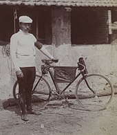Photographie en noir et blanc d'un homme se tenant debout à côté de sa bicyclette.