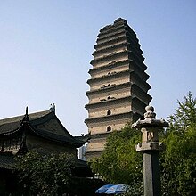 Fotografie, z podhledu, vysoké pagody, za zelení v popředí je vidět asi tucet postupně se zužujících pater; na každé straně každého patra je vysoké klenuté okno