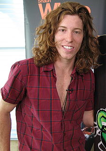 Photographie d'un homme aux cheveux longs et roux portant une chemise à carreaux.