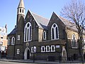The former St Barnabas Church, Kentish Town Road, Camden in London, 1884–85 by Ewan Christian, now the Greek Orthodox Cathedral of St Andrew, showing the west front with north apse and turret[157]