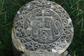 Photographie d’une stèle discoïdale en pierre, sur fond d’herbe.