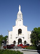 Photographie en couleurs de l'église Notre-Dame avec statue de la Vierge Marie surplombant le clocher et l'entrée.