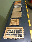Museum samples demonstrating a 1590s bed: the bedcords, bedmat, three tick mattresses in dun and striped ticking, and the bedlinen.