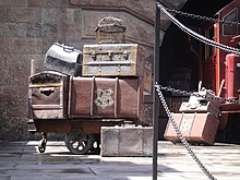 Un chariot encombré de valises dont l'une d'elles porte un blason