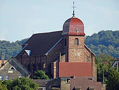 Église en grès rose de trois quarts. Successivement : un clocher comtois en tuiles vernissées rouges, chevet sans transept.