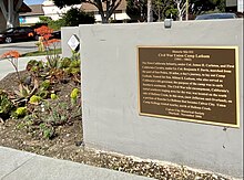 Blossoming aloe plants beside brown and gold commemorative plaque on low wall