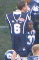 UConn Huskies football uniform with number 6 held up by another uniformed player on the sideline